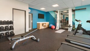 Een sportschool met loopbanden, gewichten, een bank, een halterrek en fitnessballen.