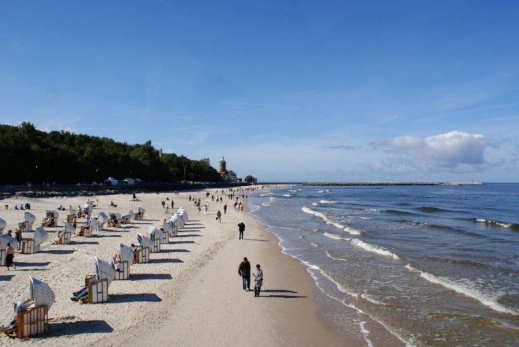 A beach with rows of sun loungers and a lighthouse in the background.