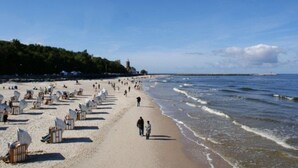 Una spiaggia con file di lettini e un faro sullo sfondo.