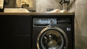 Una lavanderia piccola e moderna, con una lavatrice a carica frontale, uno specchio grande e un porta asciugamani.