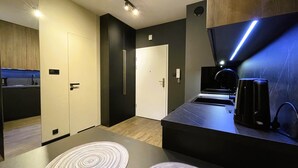 Una cucina moderna con un piano di lavoro scuro, una macchina per il caffè e un forno integrato. Ci sono due porte, una che dà sul bagno e l'altra sulla camera da letto.