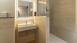 A modern bathroom with a glass-enclosed shower, a white sink with a mirror above it, and beige tiled walls. - Sure Hotel by Best Western Caen Memorial (Caen)