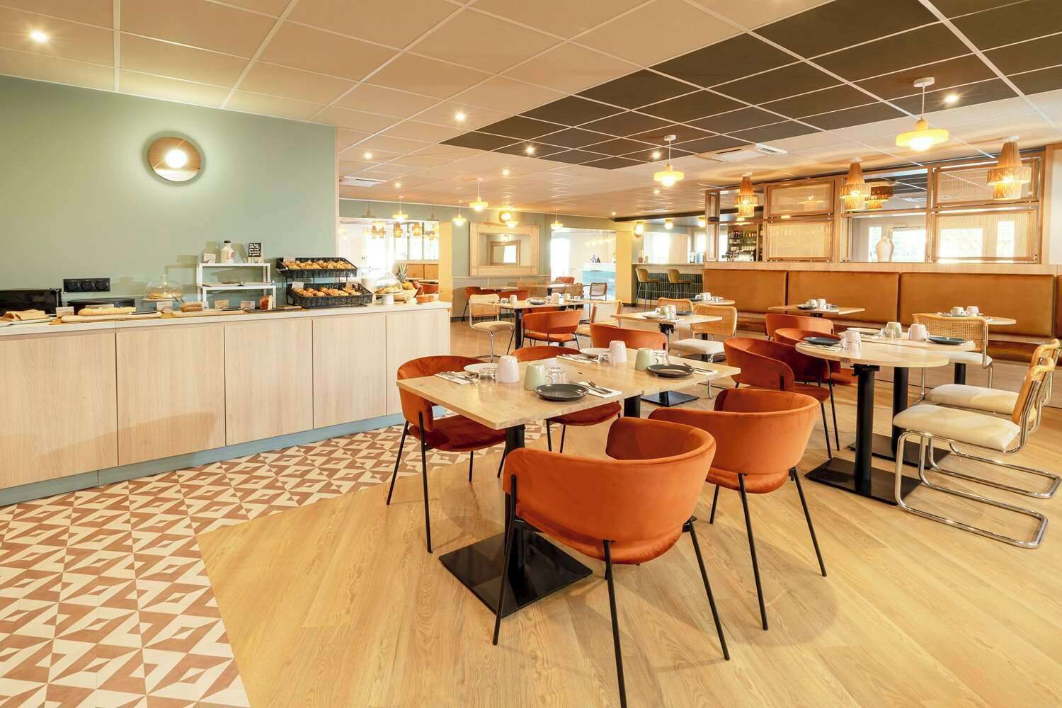 Un restaurant moderne avec un comptoir central, plusieurs tables et des chaises orange.