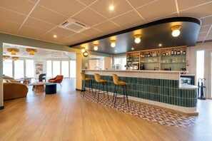 A modern bar area with a curved counter, multiple stools, and a variety of bottles and glasses on shelves. - Sure Hotel by Best Western Caen Memorial (Caen)