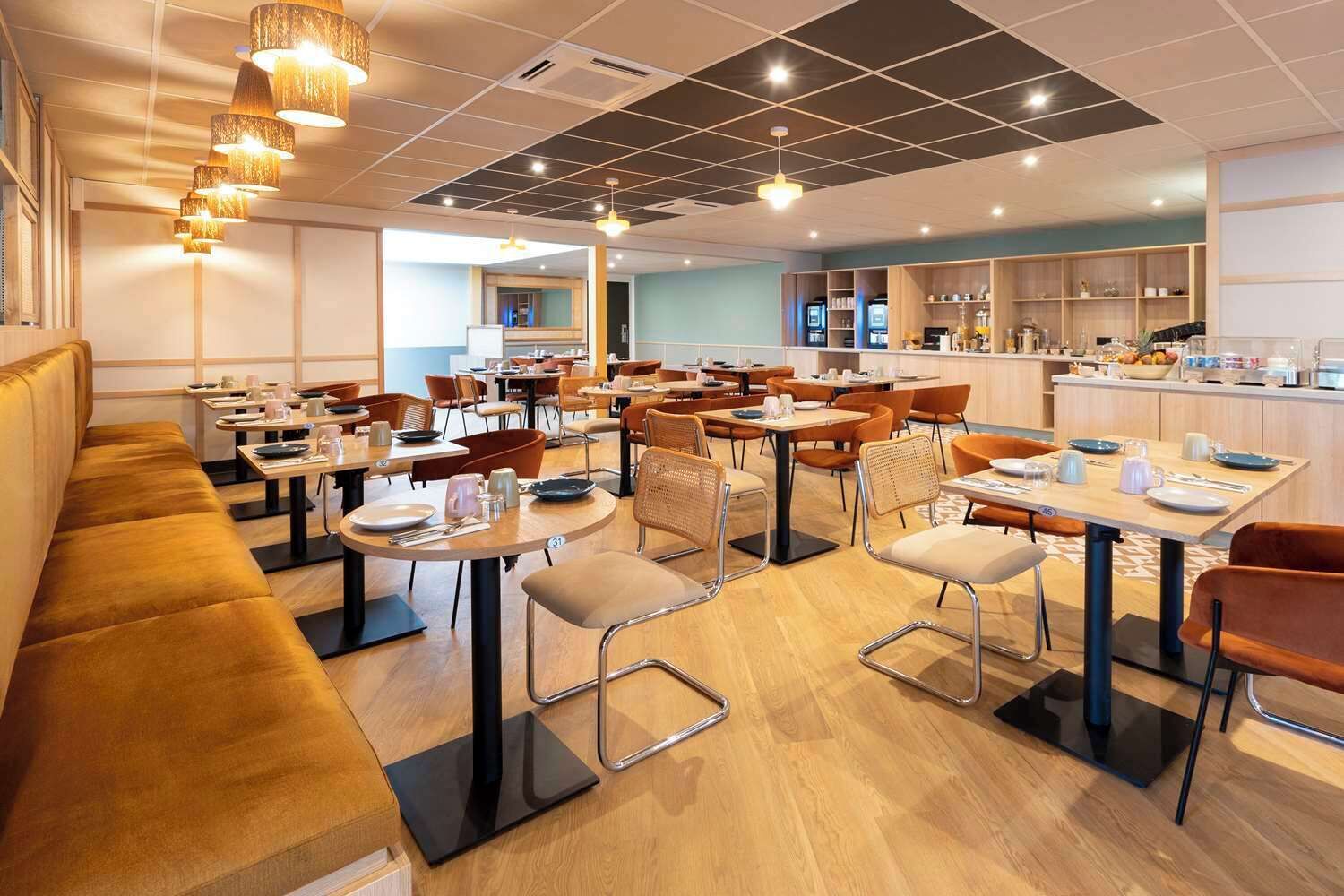 Un restaurant moderne doté de nombreuses tables et de plusieurs coins repas, d’un espace cuisine et d’un coin salon avec un canapé.