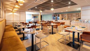 A modern restaurant with multiple dining tables and booths, a kitchen area, and a seating area with a sofa. - Sure Hotel by Best Western Caen Memorial (Caen)