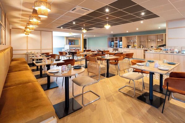 Ein modernes Restaurant mit mehreren Tischen, Sitzecken, einer Küche und einer Lounge mit einer Couch.