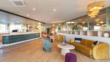 Een modern interieur met een receptiebalie, zithoek en grote ramen.