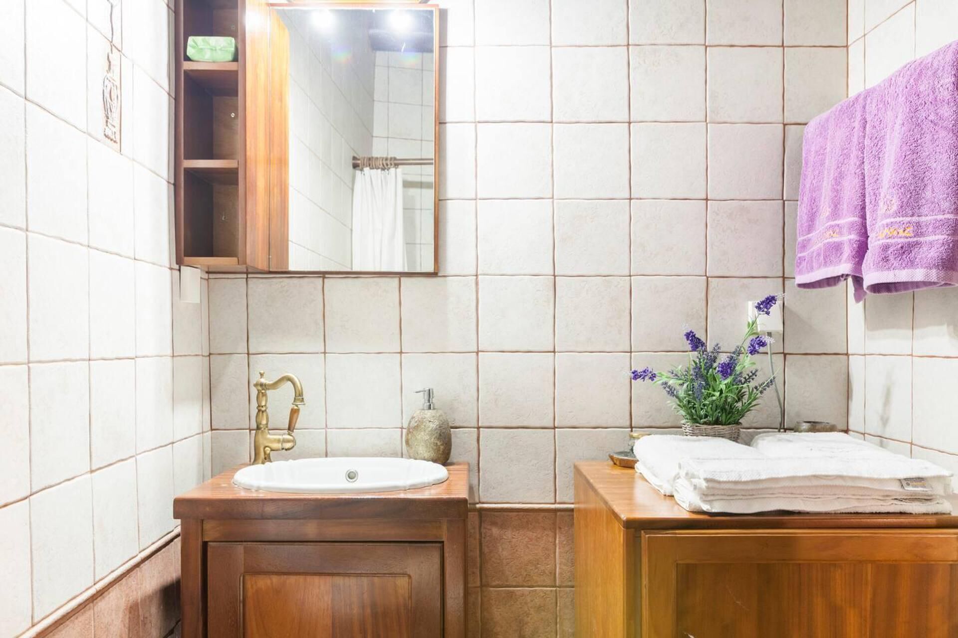 A bathroom with a wooden vanity, a sink, a mirror, and a purple towel hanging on the wall.