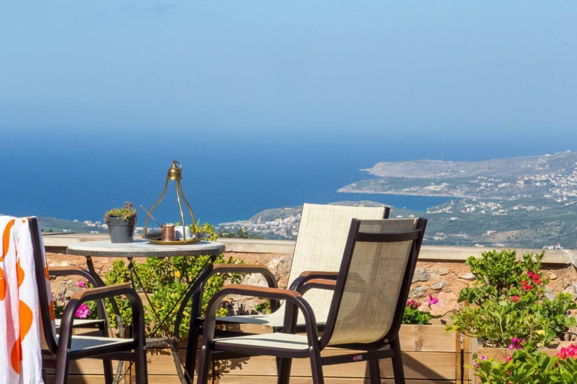 A terrace with a table and chairs overlooking a coastal view.