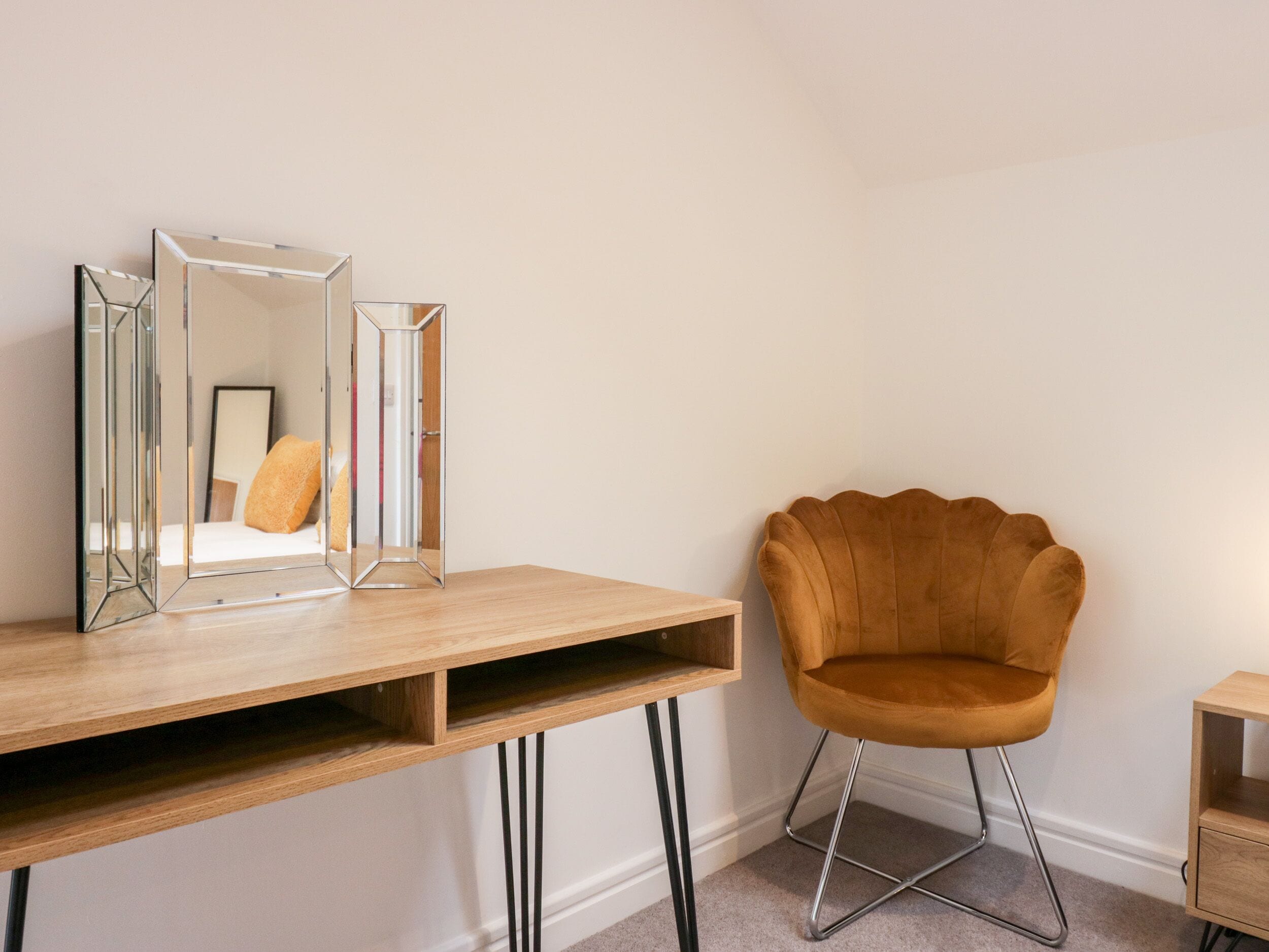 A room with a wooden desk, a mirror, a brown chair, and a small wooden cabinet.