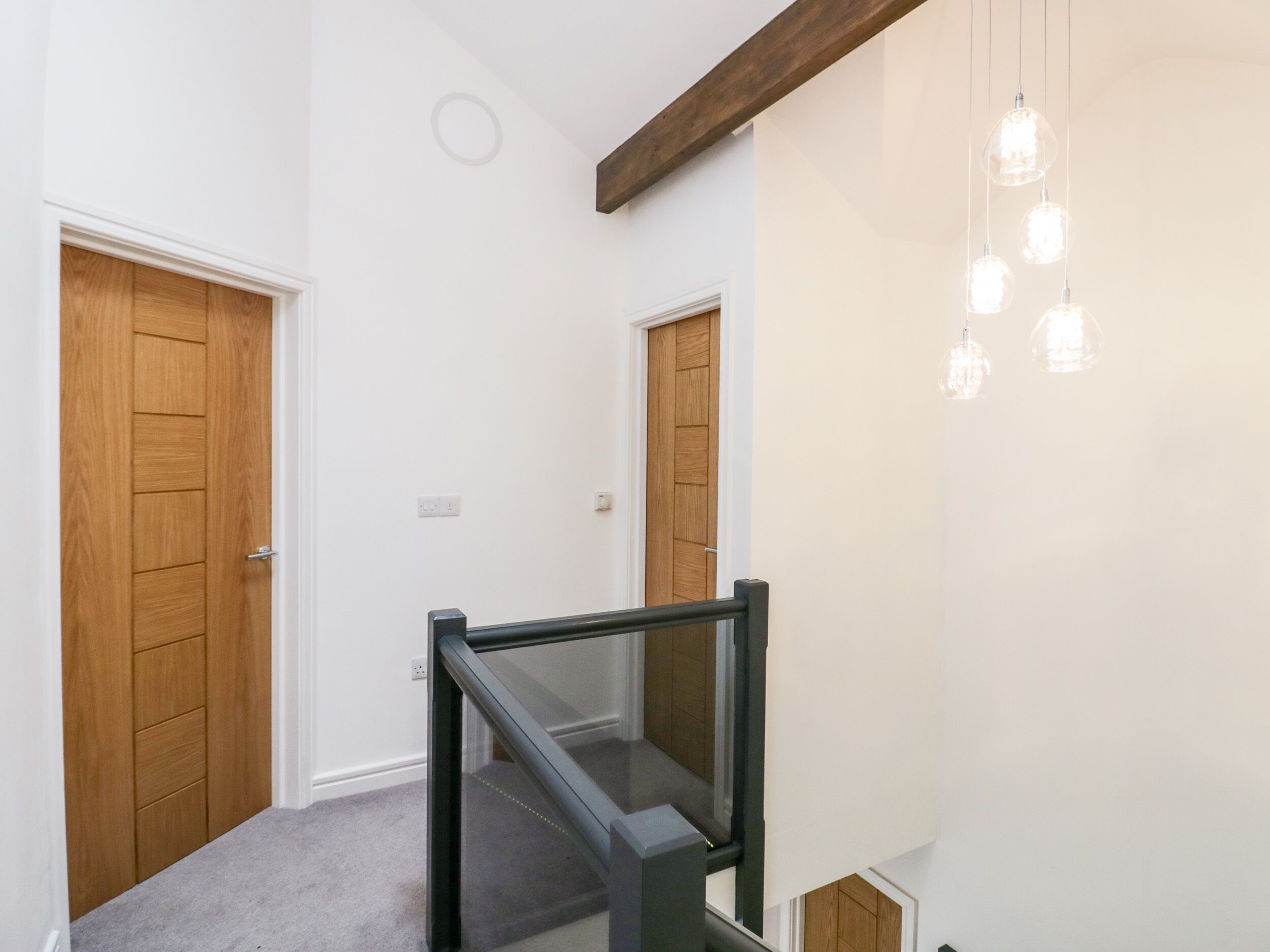 A staircase with glass railings leading to a landing, flanked by wooden doors and a hanging light fixture.