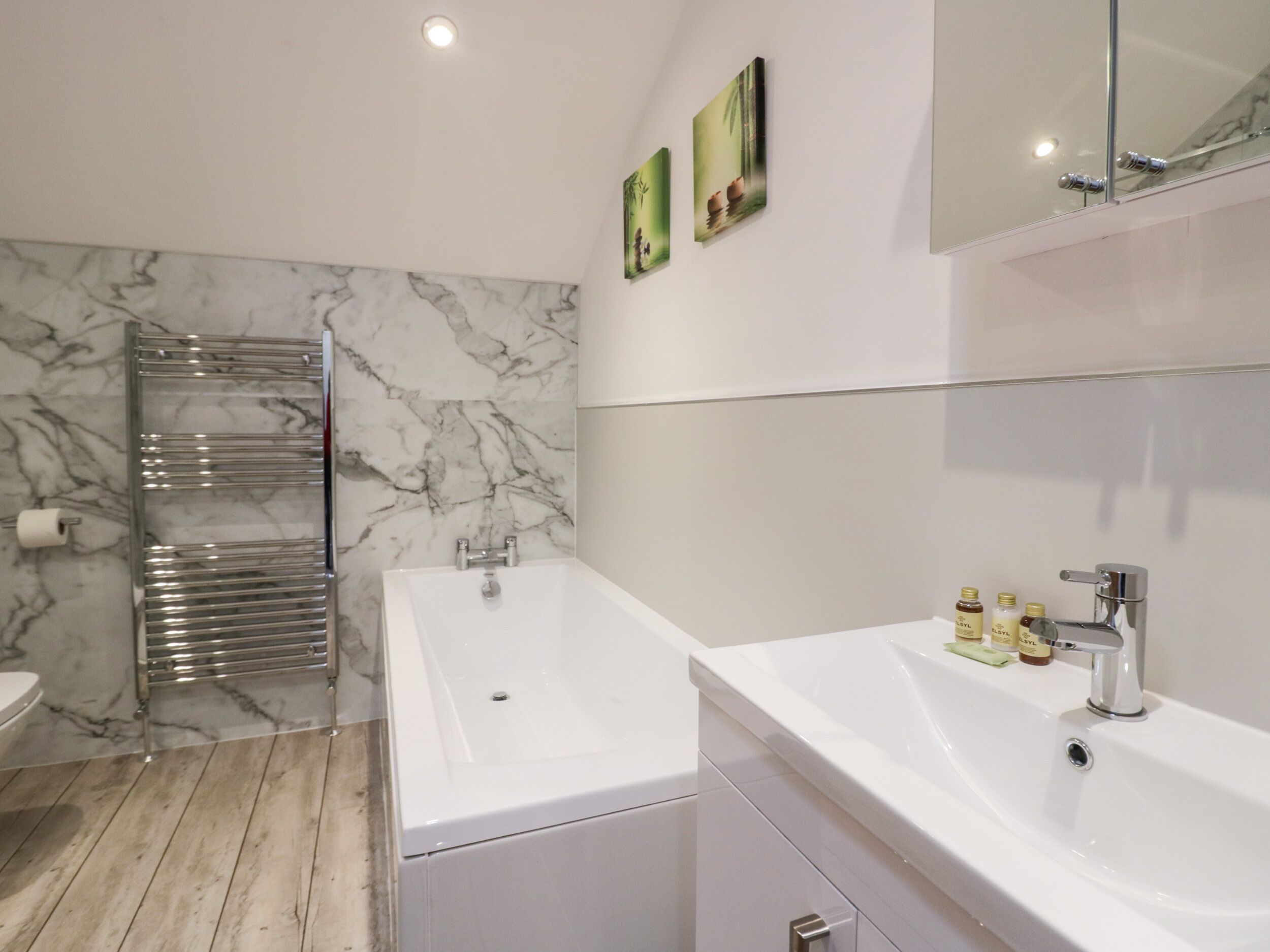 A modern bathroom with a marble wall, a glass shower enclosure, a white bathtub, and a sink with toiletries.