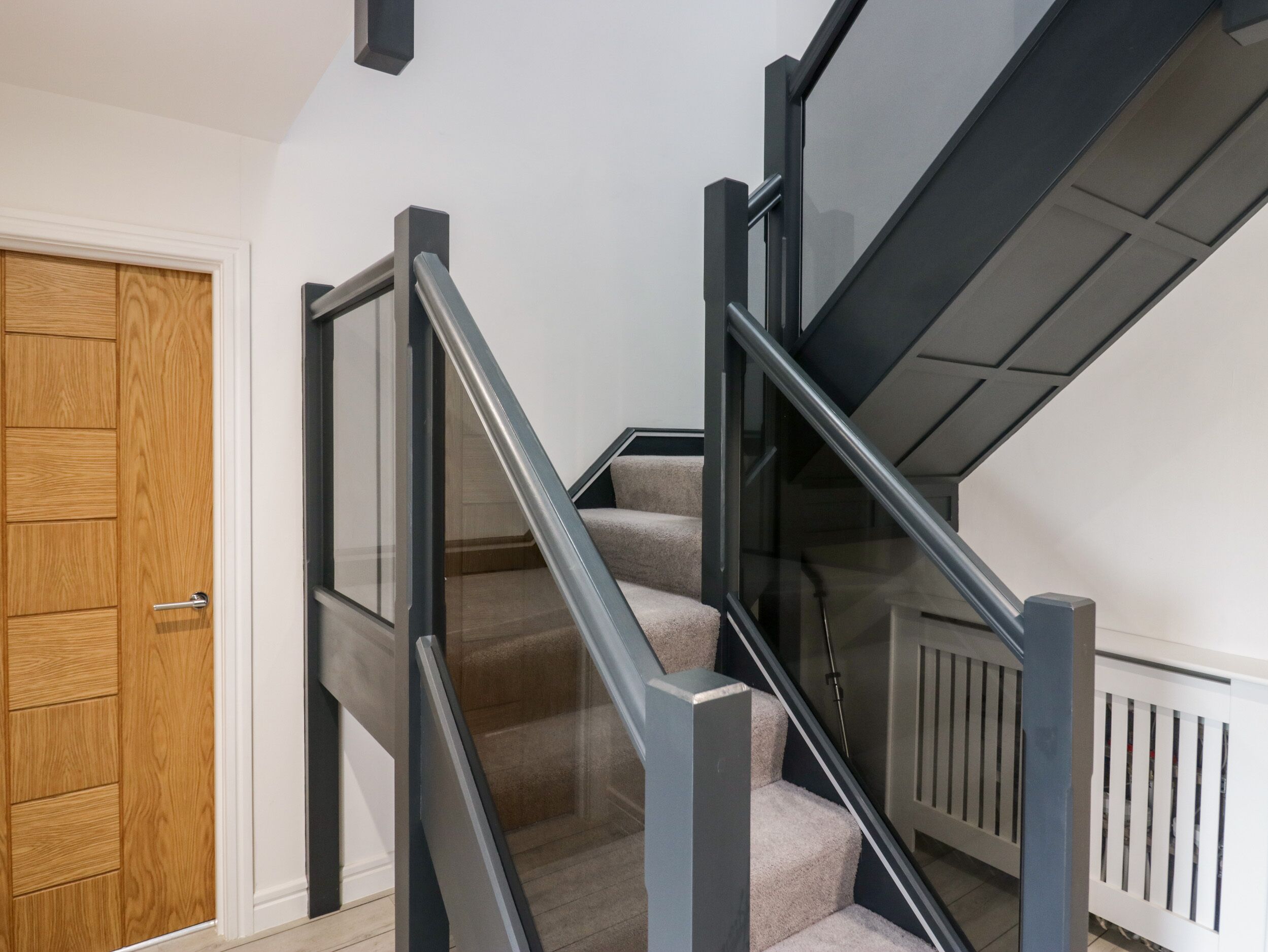 Una escalera moderna con barandillas de vidrio y peldaños alfombrados en color beige.