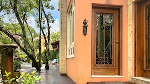 A wooden door with a wrought iron gate, a potted plant, and a bench in a covered outdoor area with a brick wall and a pool in the background. - Casa Alto Padrão na Granja Viana - Cond. Fechado (Carapicuiba)