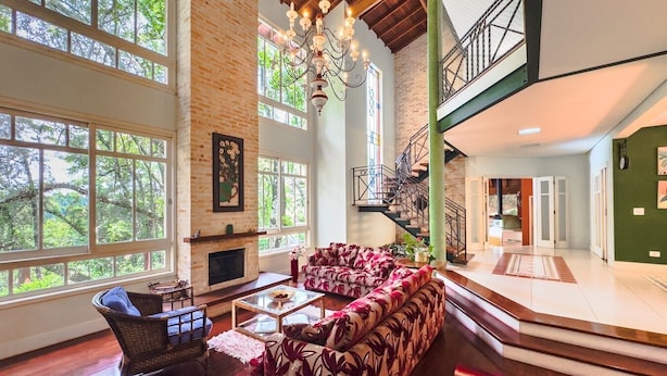 A spacious living area with a fireplace, large windows, and a staircase leading to an upper level. - Casa Alto Padrão na Granja Viana - Cond. Fechado (Carapicuiba)