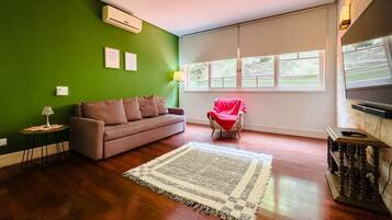 Un salon avec un mur vert, un canapé marron, un fauteuil rouge, une grande fenêtre et un téléviseur à écran plat.