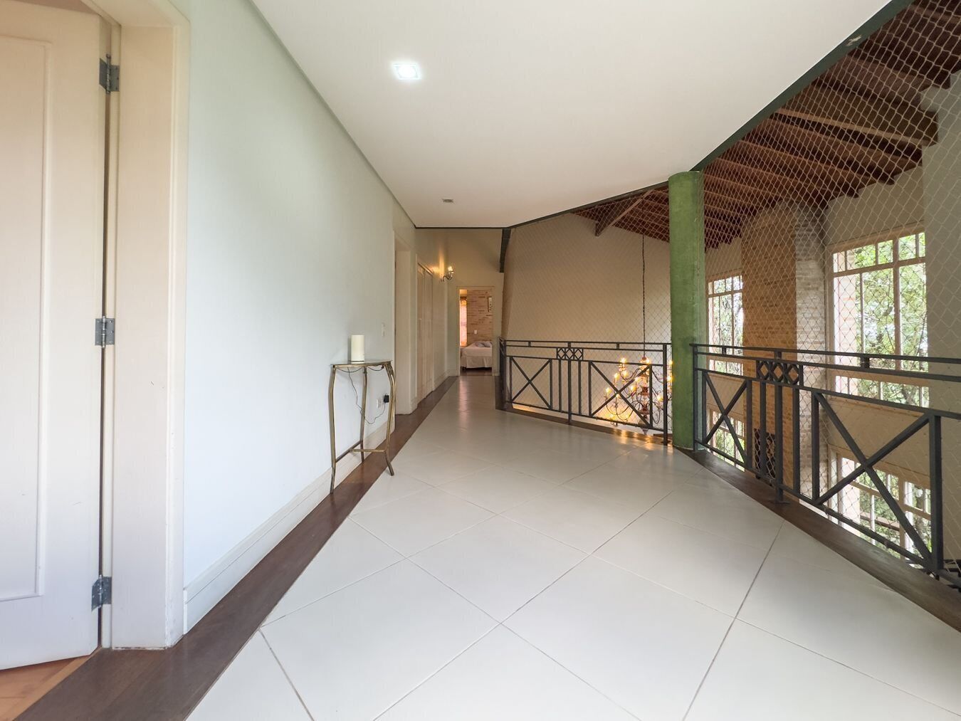 A spacious corridor with a high ceiling, a metal railing along the right side, and a door on the left.