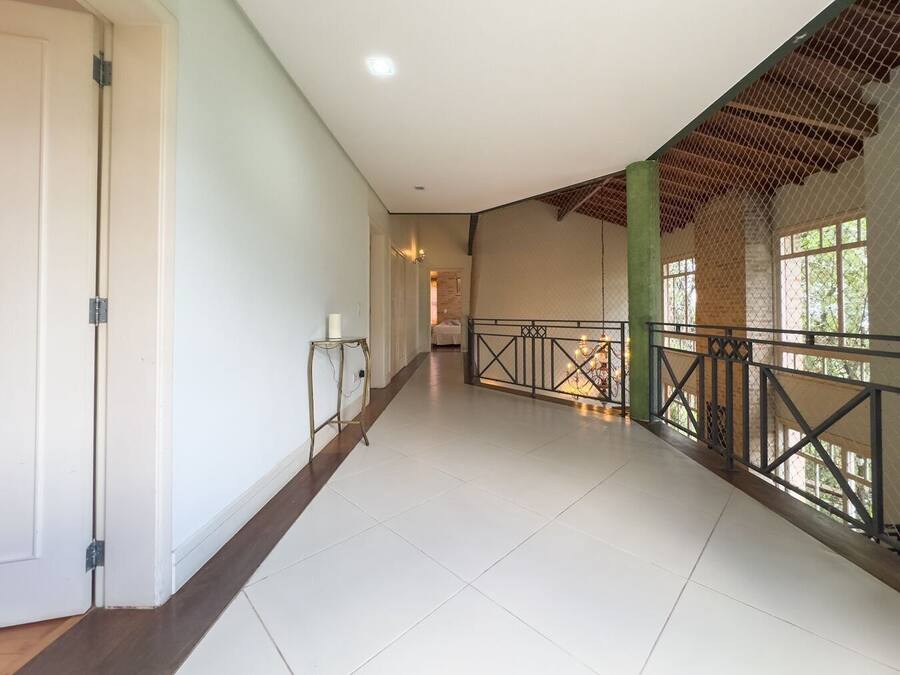 A spacious corridor with a high ceiling, a metal railing along the right side, and a door on the left.