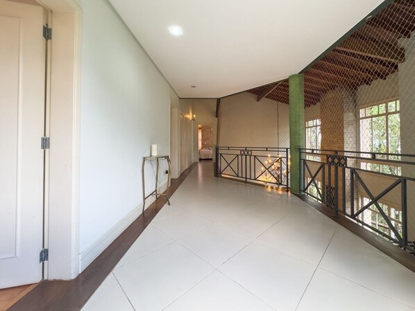 A spacious corridor with a high ceiling, a metal railing along the right side, and a door on the left. - Casa Alto Padrão na Granja Viana - Cond. Fechado (Carapicuiba)
