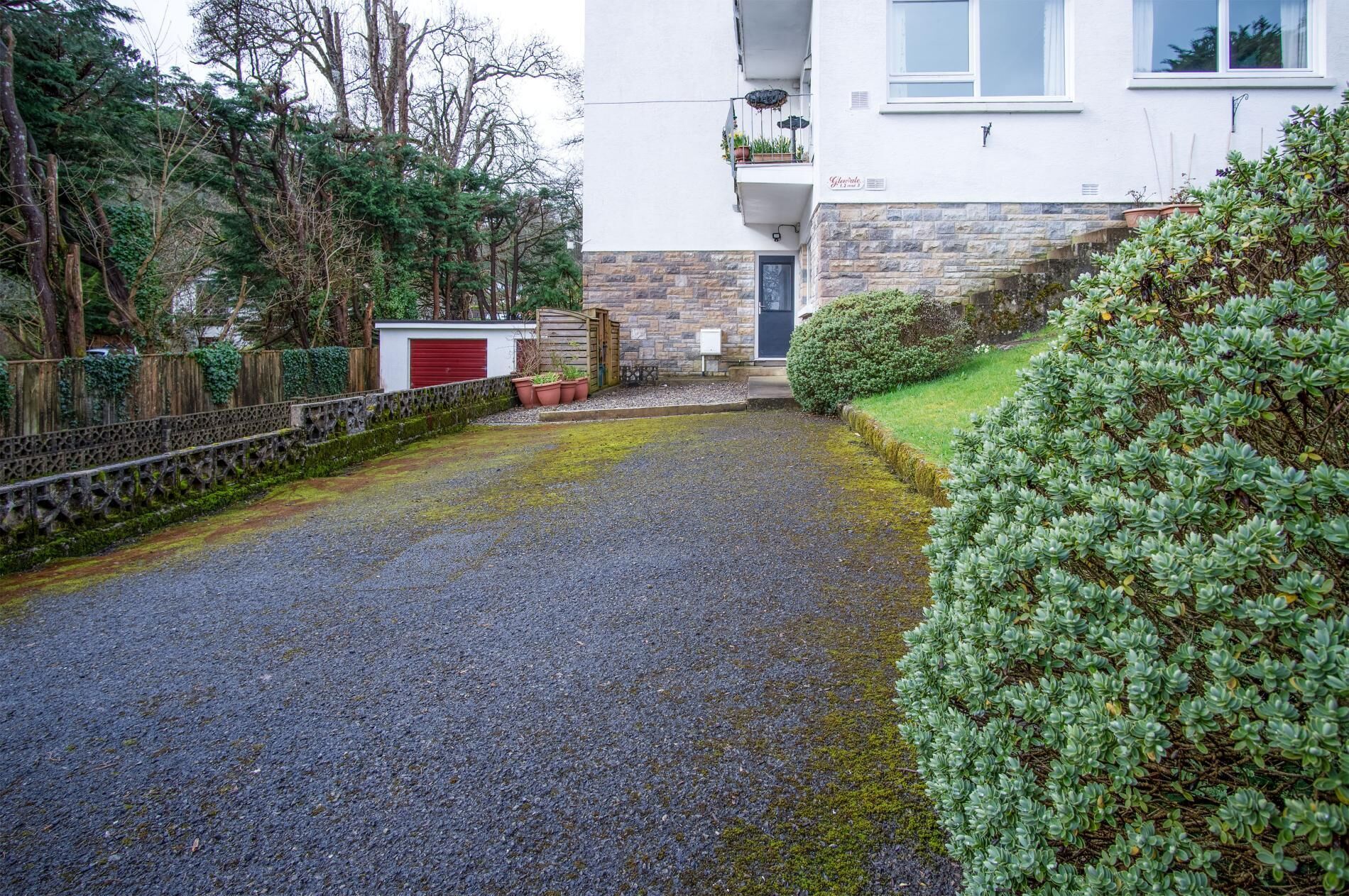 A residential area with a gravel driveway leading to a house with a stone facade and a red garage door.