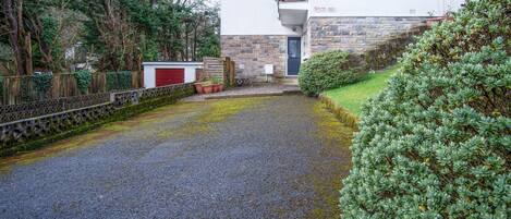 A residential area with a gravel driveway leading to a house with a stone facade and a red garage door.