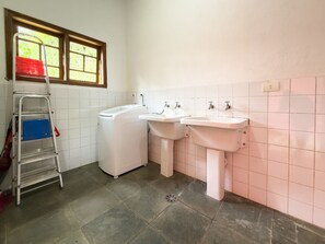 Ein Badezimmer mit Waschmaschine, zwei Waschbecken, einer Leiter und einem Fenster mit Blick auf Grünflächen.