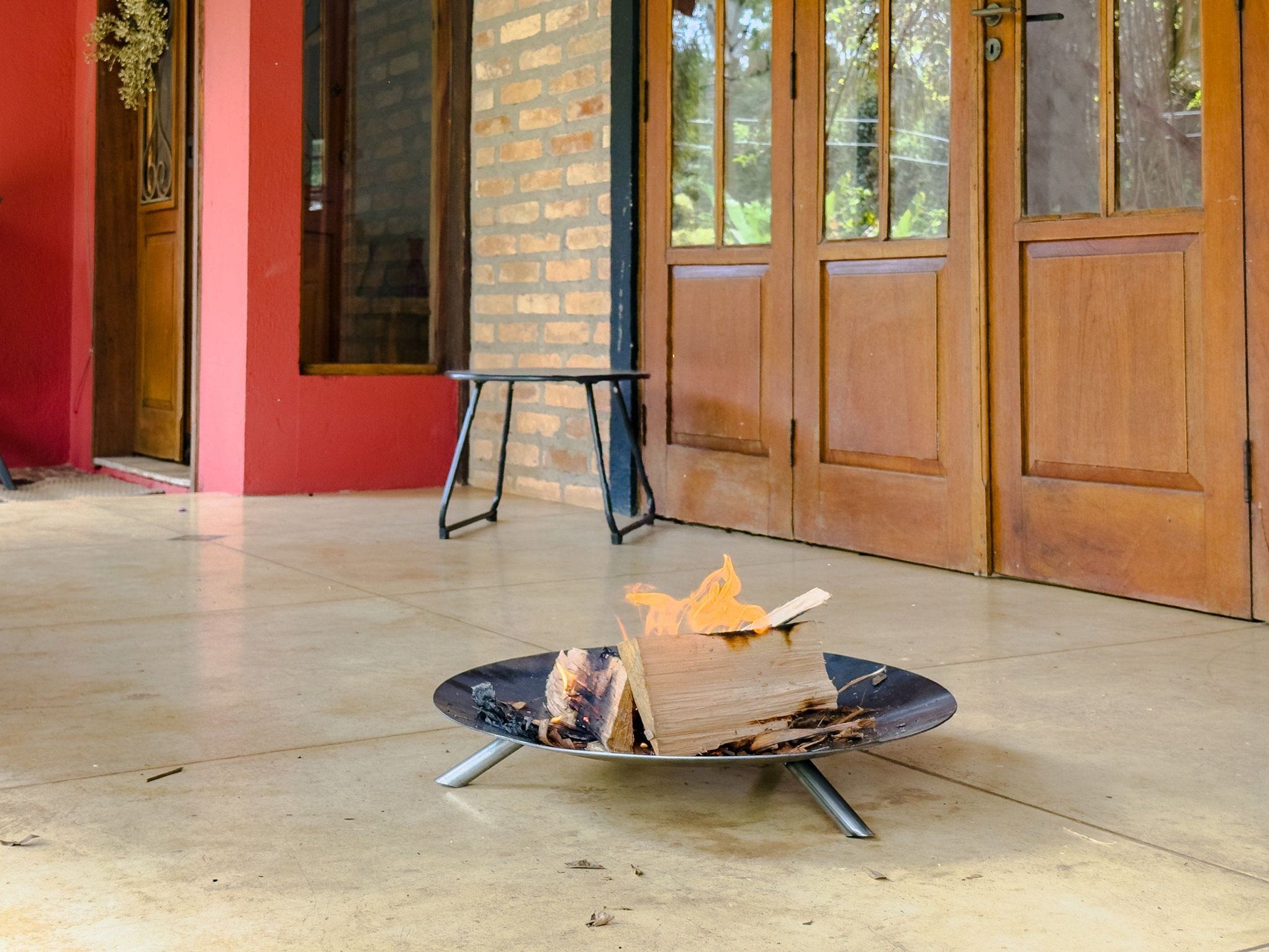 A fire pit with burning wood in a covered outdoor area with a brick wall and wooden doors.