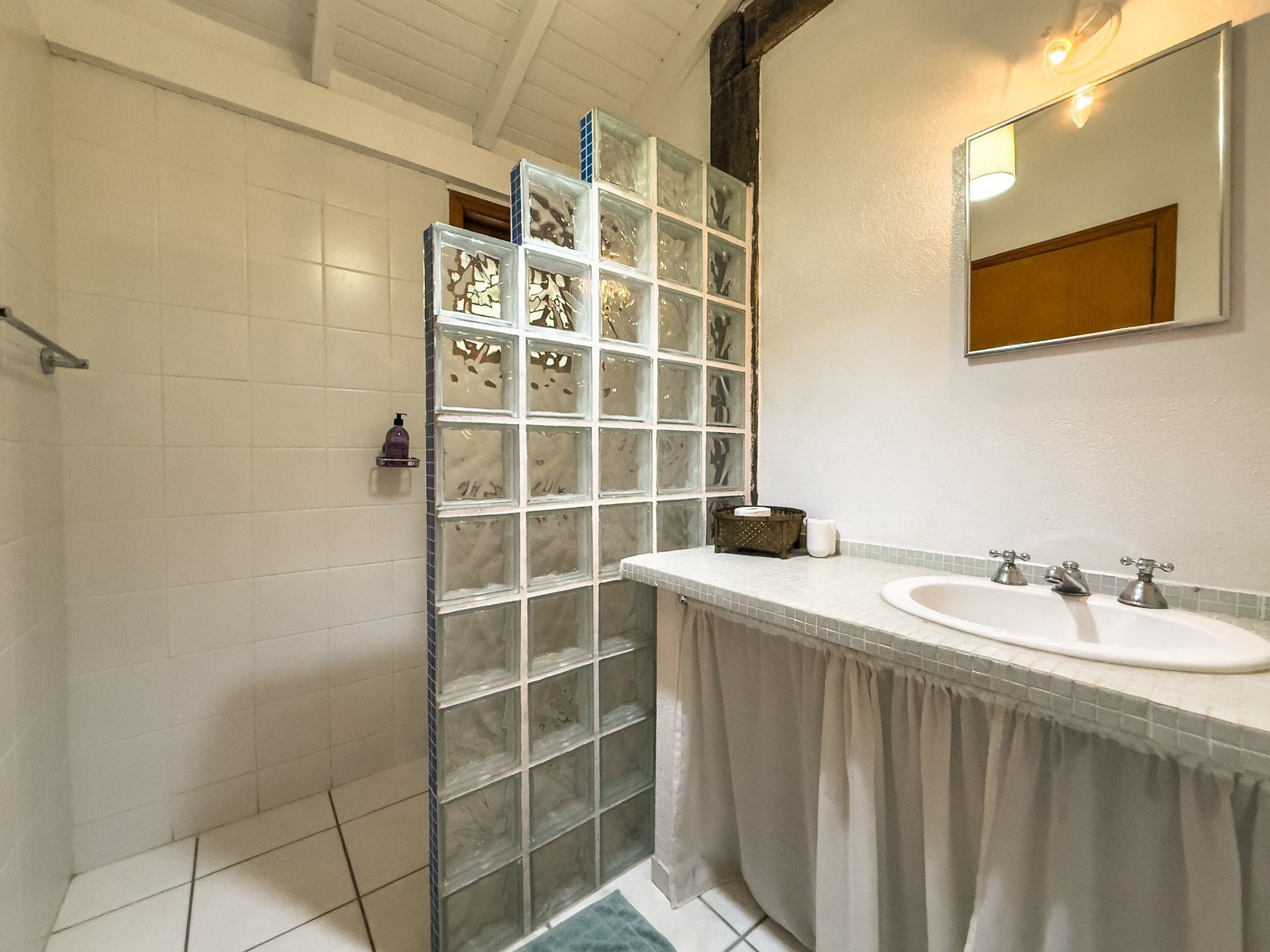A bathroom with a glass shower enclosure, a sink with two faucets, and a mirror above the sink.