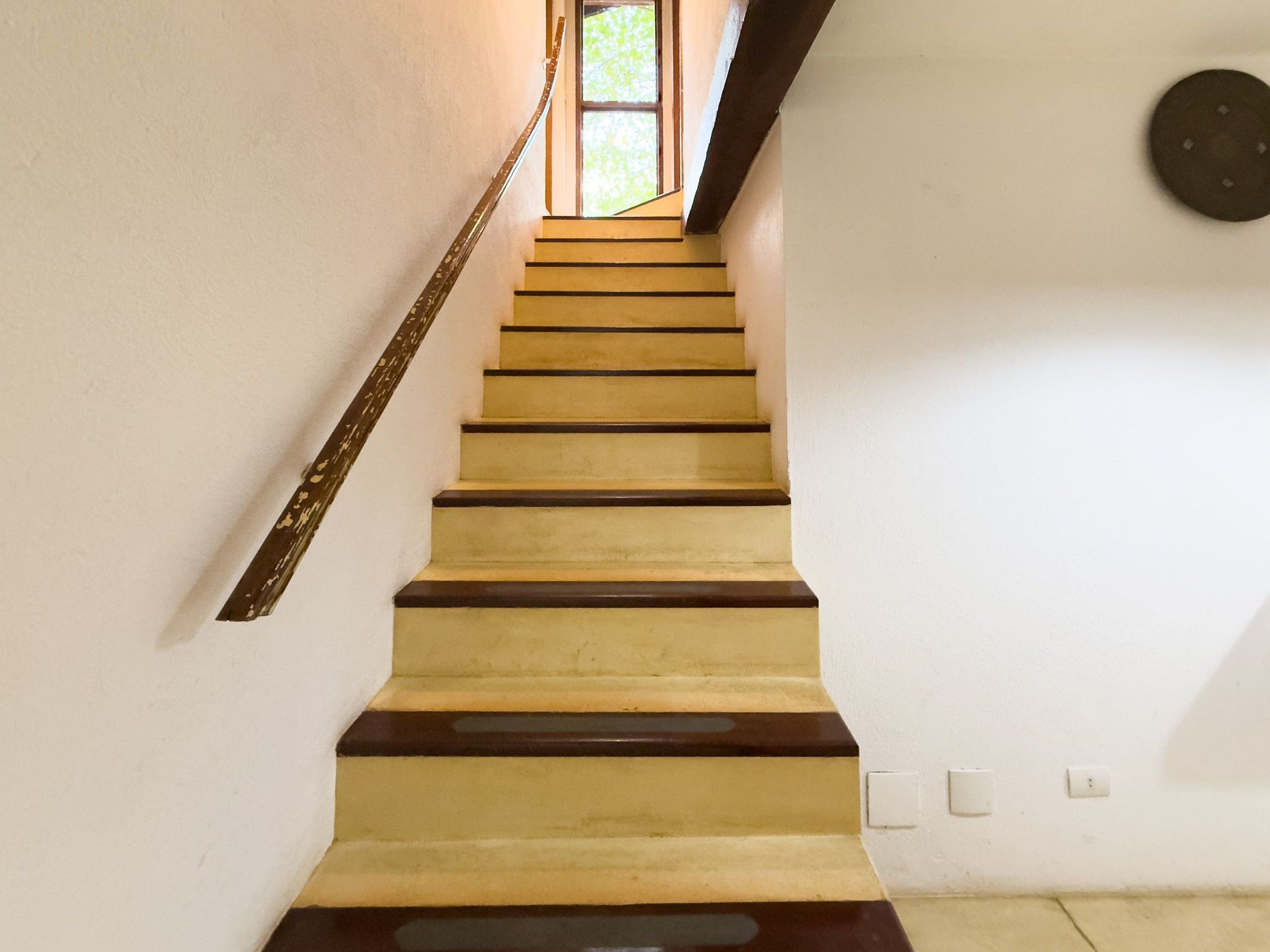 Eine Treppe mit abwechselnd gelben und dunkelbraunen Stufen, die zu einem Fenster mit Blick auf Grünanlagen führt.