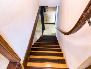 Un escalier en bois, doté d’une rampe, mène à une pièce dont le sol est recouvert de carreaux.