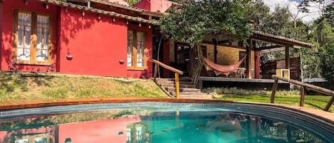A red house with a swimming pool, a hammock, and a wooden deck.