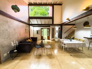 Un vaste espace de vie comprenant un canapé aux couleurs sombres, une table à manger pour quatre personnes et un escalier menant à un niveau supérieur.