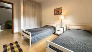 Une chambre avec deux lits, une table de chevet avec une lampe, un tapis à motifs et un rideau.
