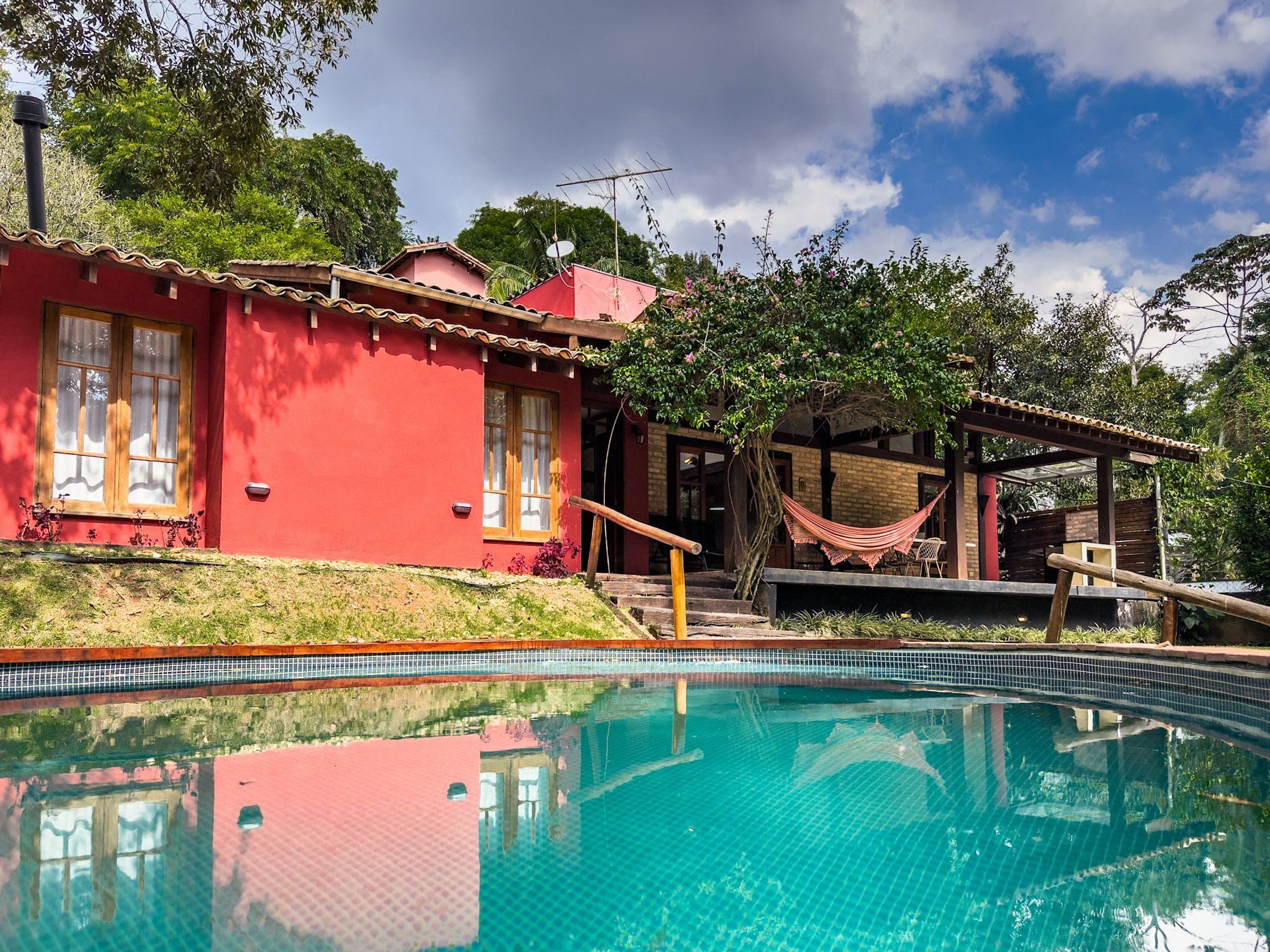 A red building with a pool, a hammock, and a wooden structure.