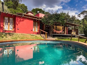 A red house with a swimming pool, a hammock, and a wooden deck.