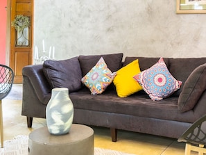Un canapé marron agrémenté de coussins aux motifs colorés, un vase posé sur une table ronde et une porte décorée d’une guirlande.