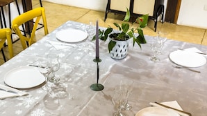 Une table à manger dressée avec de l’assiette blanche, des couverts et des verres à vin transparents, entourée de chaises.