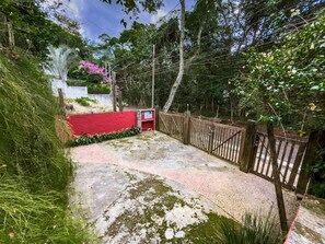 Un chemin pavé mène à une zone délimitée par un portail, un mur rouge et une clôture en bois.