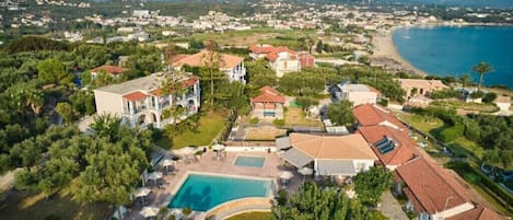 An aerial view of a coastal resort with a swimming pool, villas, and a beach.
