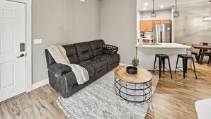 A living room with a leather sofa, a round coffee table, and a kitchen area in the background.