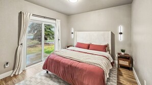 A bedroom with a large bed, a nightstand, a window with curtains, and a ceiling light.
