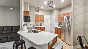 A modern kitchen with a central island, stainless steel appliances, wooden cabinets, and pendant lighting.