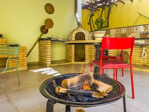 Ein gemütlicher Außenbereich mit Feuerschale, einem roten Sessel und einem Backofen aus Ziegeln.