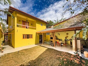 A two-story yellow house with a patio, a brick fireplace, and a small garden. - Espaço gourmet e home-office na Granja Viana (Carapicuiba)
