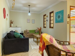 Sala de estar com sofá, poltrona e uma pequena mesa. Há duas janelas com molduras de madeira e um quadro na parede.