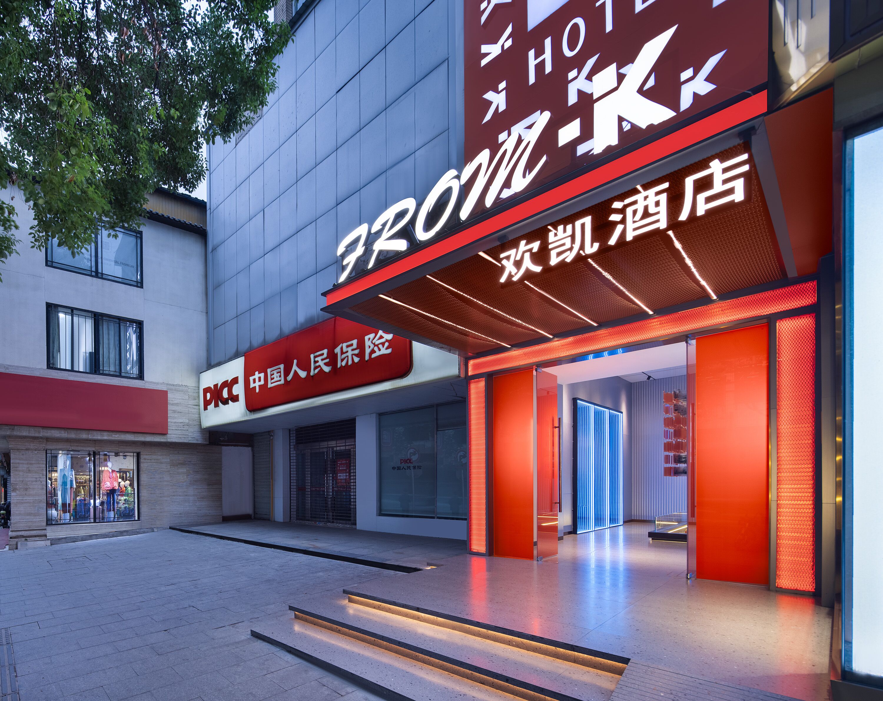 Entrada de hotel com design moderno, destacando uma placa com caracteres chineses e um toldo vermelho.