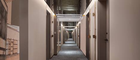 A long, narrow hallway with doors on both sides, a patterned floor, and a ceiling with a unique design.