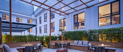 A modern outdoor patio with seating, tables, and a glass ceiling structure.