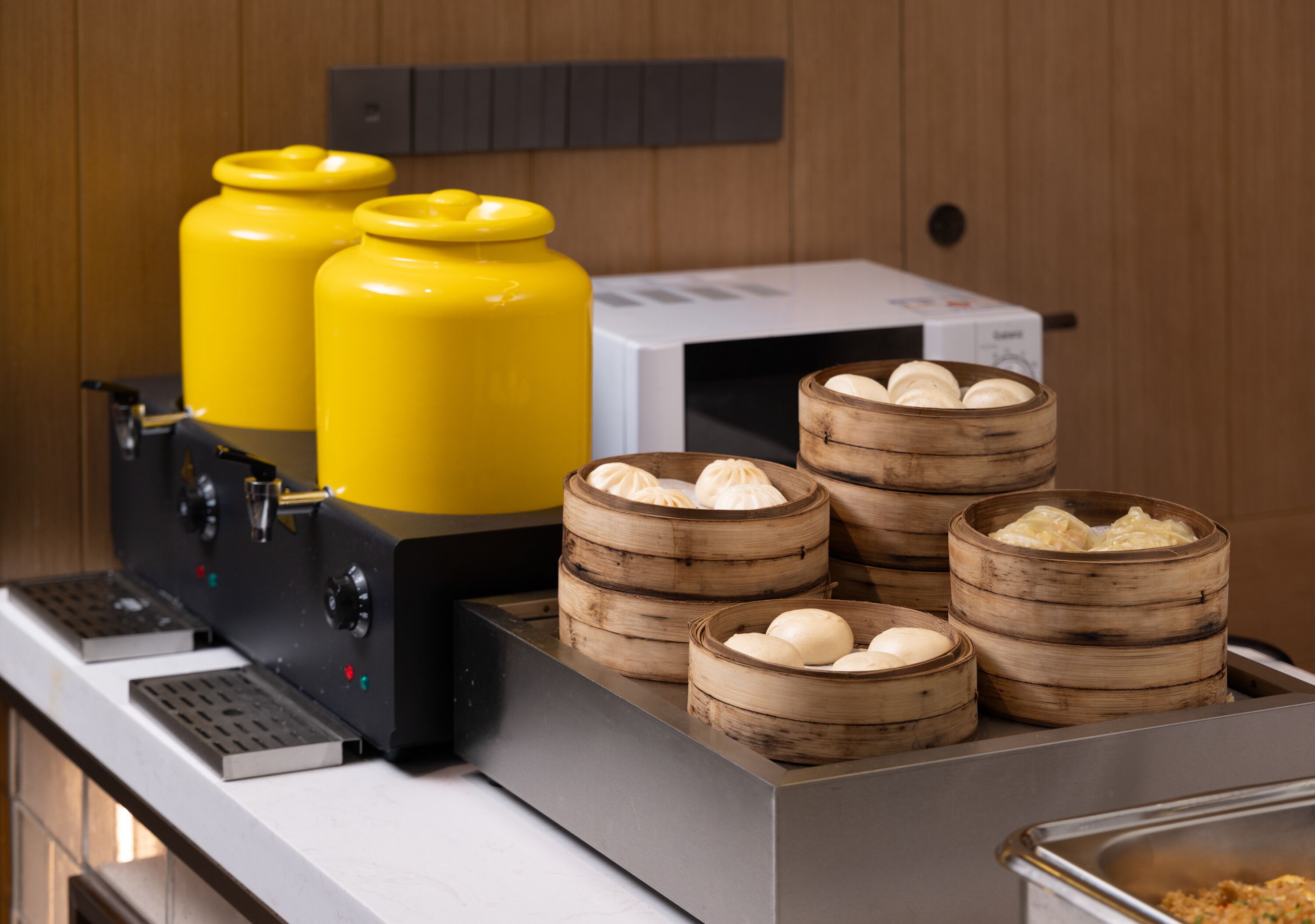 A kitchen area with a coffee machine, two yellow gas cylinders, and several bamboo steamers with dumplings.